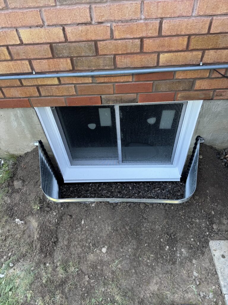 Black casement egress window in a steel well, exterior view, Toronto