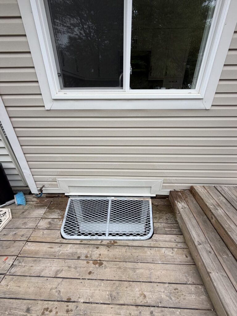 Egress window and well installed under a deck with a steel grate cover