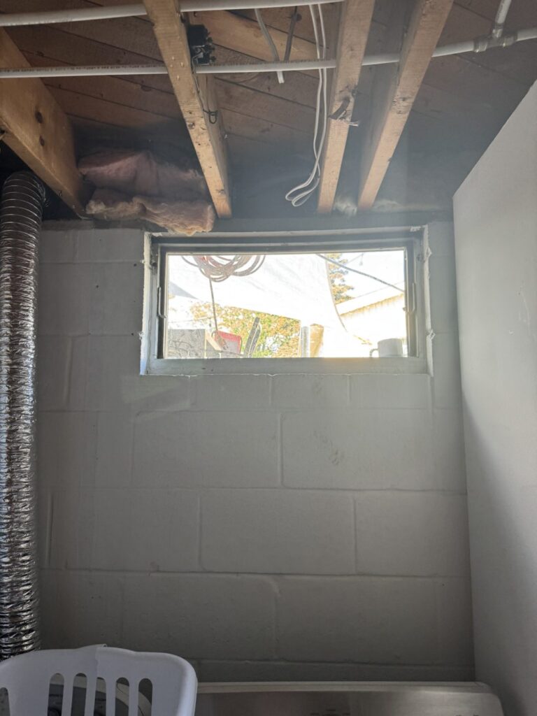 Original small basement window in a block wall before an egress cut-down, Oshawa